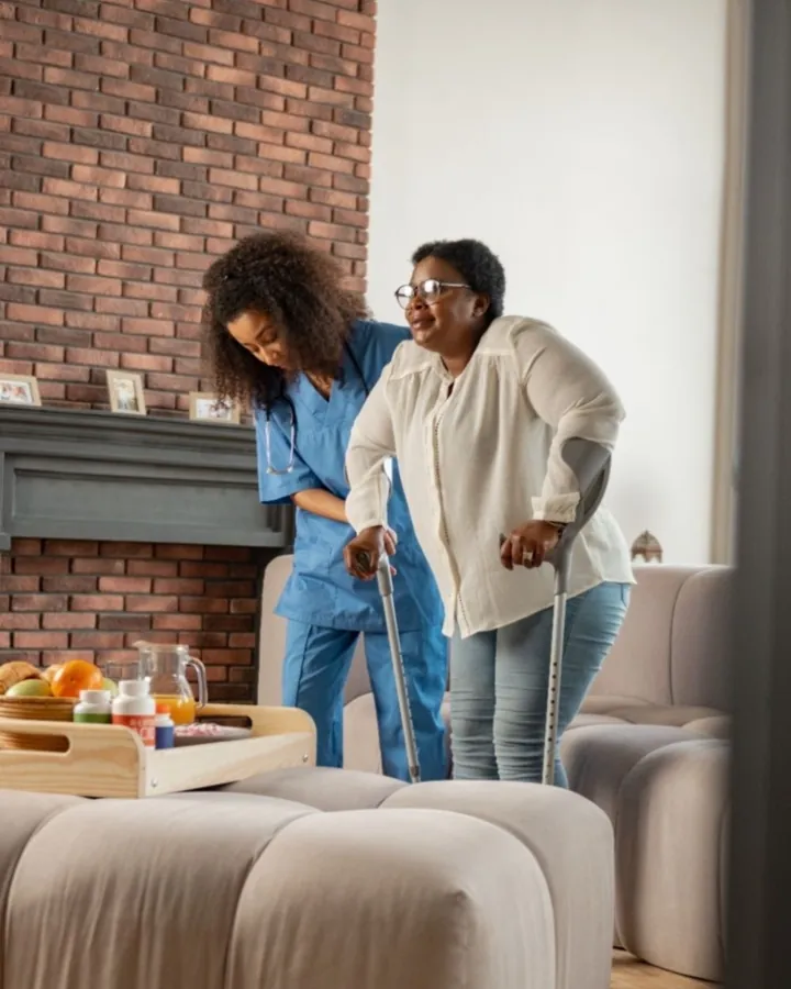 A nurse helping a woman walk with crutches at home